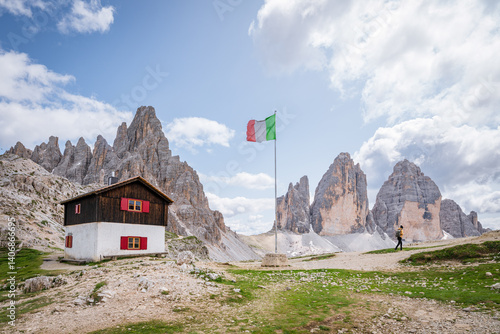 Obraz na płótnie Hiker explores the Dolomites near a public refuge and Italian flag. w salonie