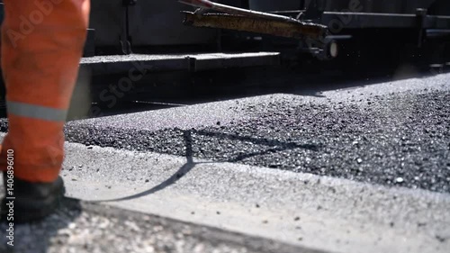 Construction worker spreading fresh asphalt with rake to ensure perfectly even finish on road construction site, close-up