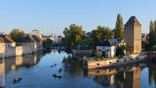 People canoeing on River Ill in city of Strasbourg at sunrise in Alsace, Grand Est, France. On the right medieval tower of Ponts Couverts - Covered Bridges.