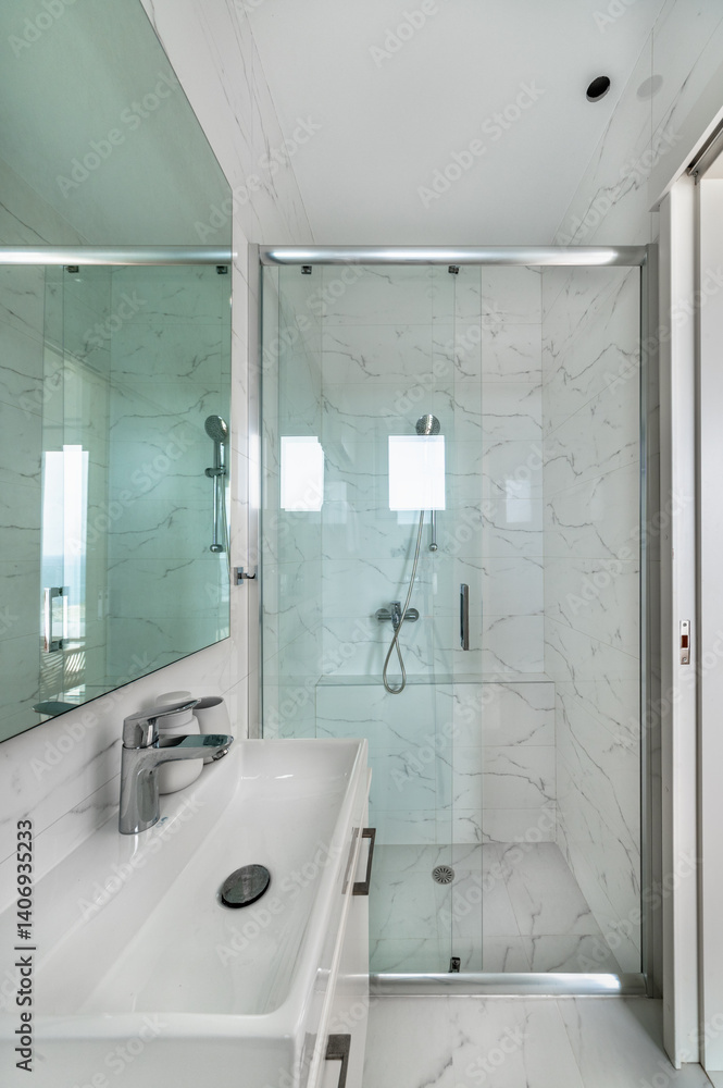 Obraz premium Modern bathroom interior in white tones, walk-in shower with glass partition and sliding door, white sink with mirror above, marble tiles, clean elegant design, bright minimalist space.