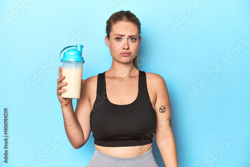 Billede på lærred Sporty blonde with a protein shake in a studio confused, feels doubtful and unsure