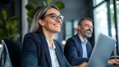 Two people in suits are sitting at a table with a laptop open in front of them