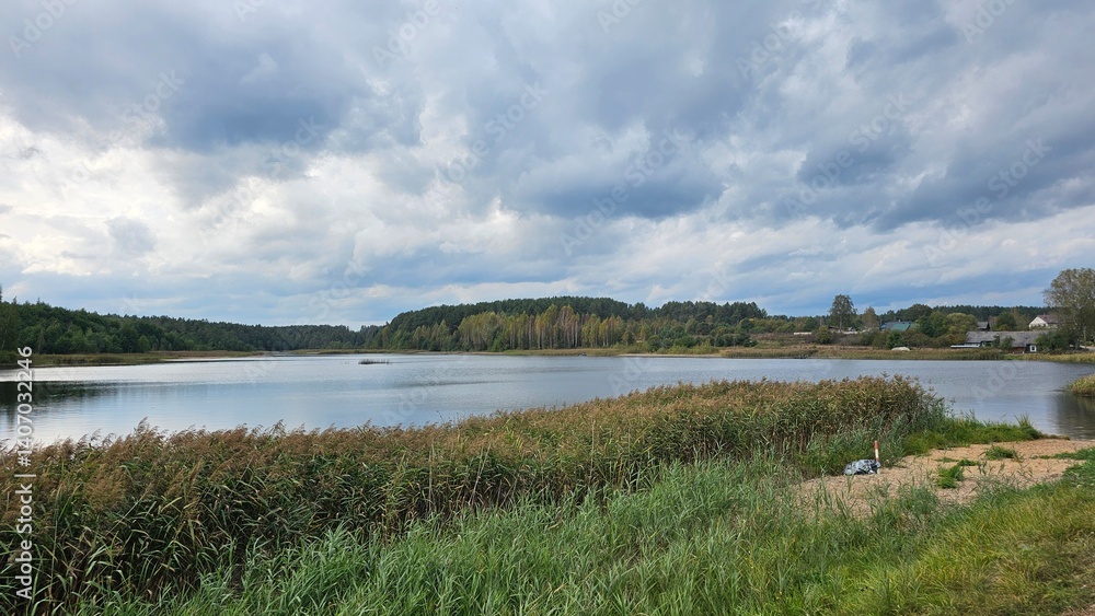 Photo of lake in the small village in Belarus. Dark heavy clouds above the loch. Green grass Photo of lake in the small village in Belarus. Dark heavy clouds above the loch. Green grass