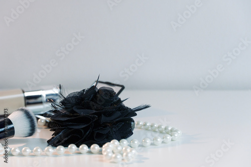 Black satin flower with pearl necklace, makeup brush and foundation in the background, beauty concept with a copy space   