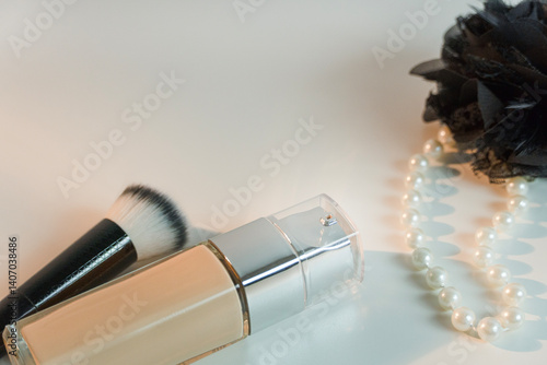 Makeup beige foundation and a brush next to a black hair clip and a pearl necklace isolated on the white background, beauty concept with a copy space  
