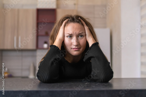 Obraz na płótnie Exhausted woman suffering from headache or chronic migraine, sitting at kitchen table and touching head with hands, feeling desperate and stressed, having psychological problem w salonie