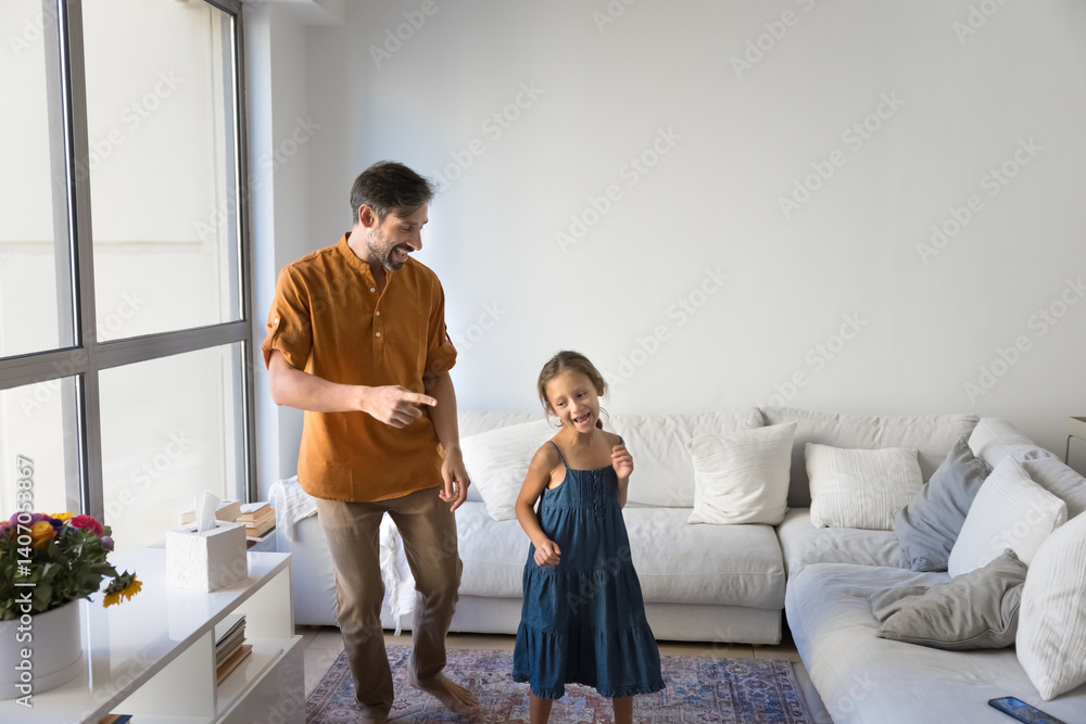 Excitement of new home. Happy joyful middle aged single dad dance barefoot with cute preteen daughter at modern designed cozy living room of new rented purchased renovated house apartment. Copy space Excitement of new home. Happy joyful middle aged single dad dance barefoot with cute preteen daughter at modern designed cozy living room of new rented purchased renovated house apartment. Copy space