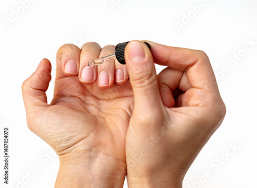 Close-up of female hand applying cuticle oil on natural nails using oil dropper.