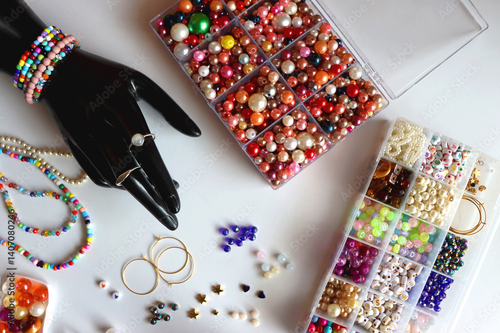 Hand figurine, colorful friendship bracelets, necklaces, various beads and DIY supplies on the table. Making jewelry at home. Flat lay.