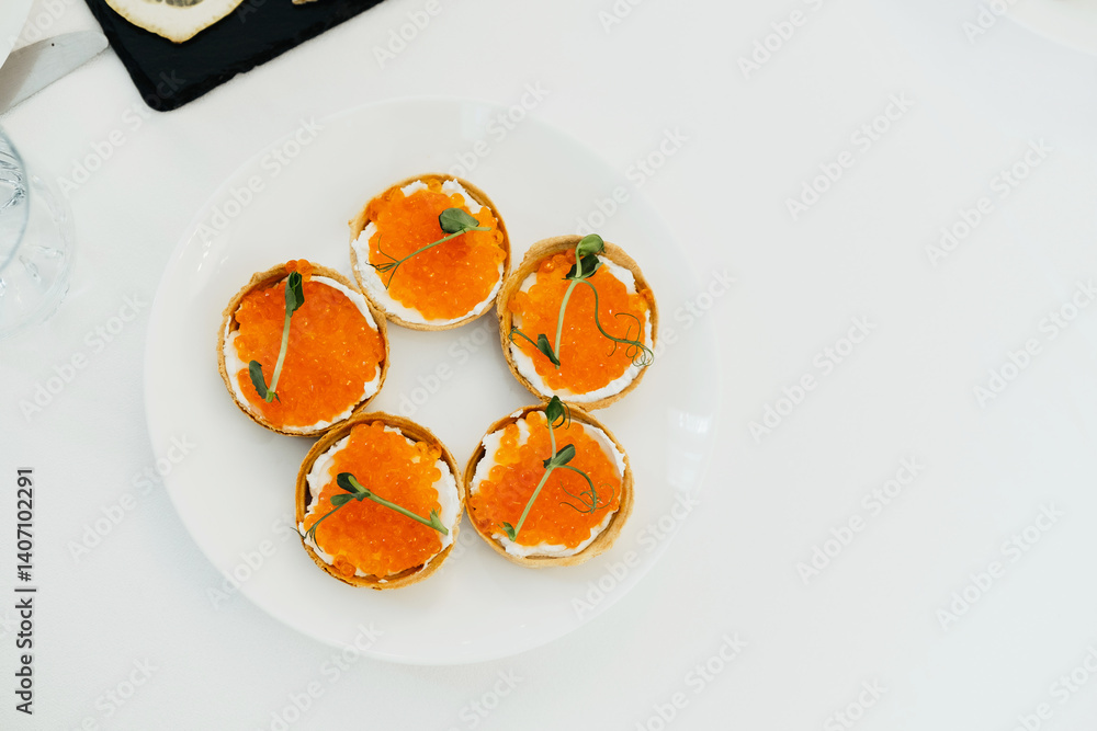 Five elegant appetizers topped with vibrant orange caviar sit on a white plate
