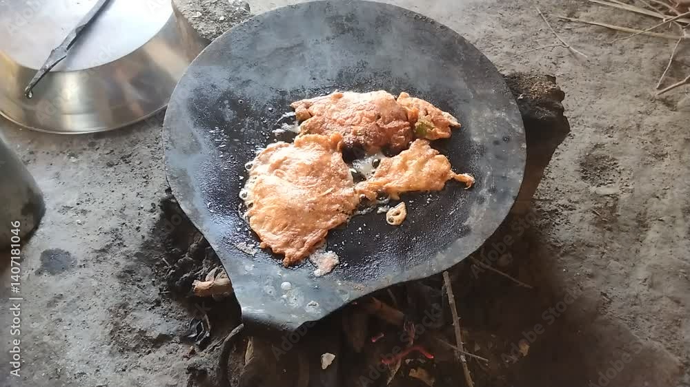 Traditional cooking of eggs on iron griddle over open fire with ghee in rural kitchen setting using firewood stove

