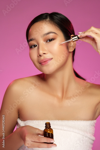 Obraz na płótnie Woman applying facial serum with a dropper while smiling against a vibrant pink background w salonie