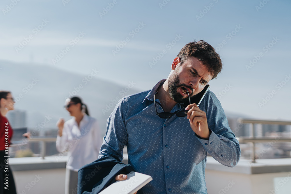 A focused businessman multitasks outdoors, holding a phone and chewing on his glasses. Colleagues engage in the background, depicting a busy professional environment.