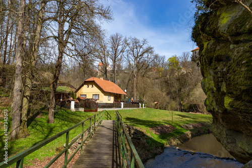 Obraz na płótnie House by a stream near high cliffs. Warm spring day. w salonie