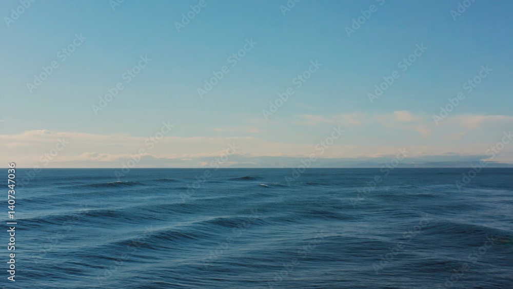 Fototapeta premium Serene view of a calm ocean at sunset, with the horizon line visible and clear blue skies. Ideal for relaxation or vacation photography.