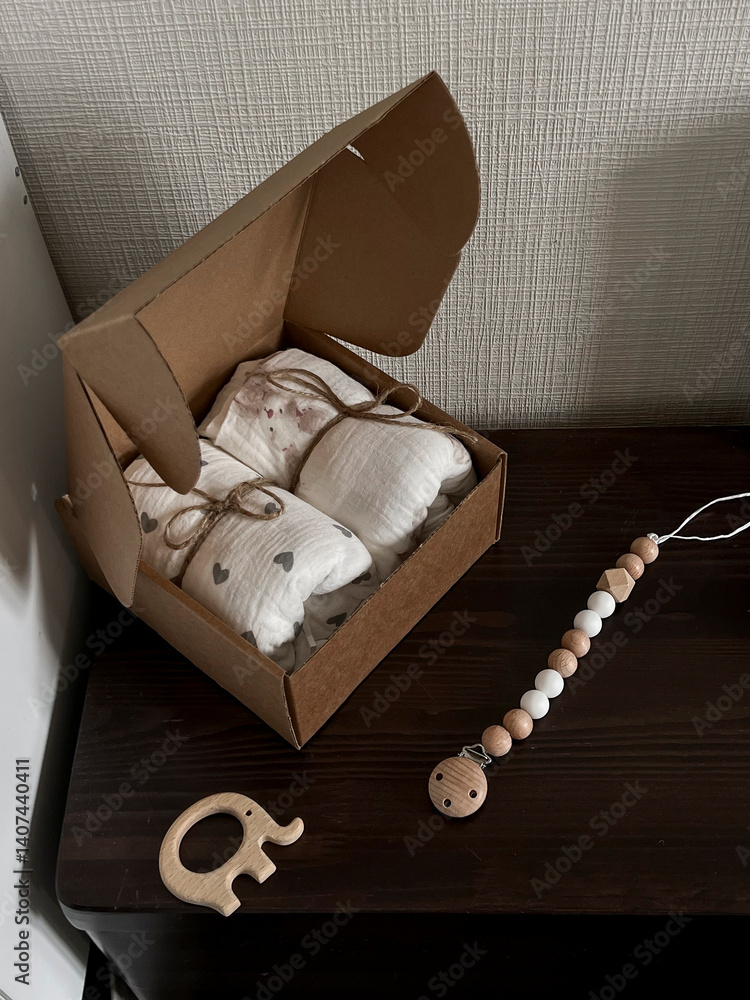 A box of muslin diapers, beads, and a wooden elephant teether are on the bedside table. Fashionable Scandinavian accessories for newborns on the bedside table