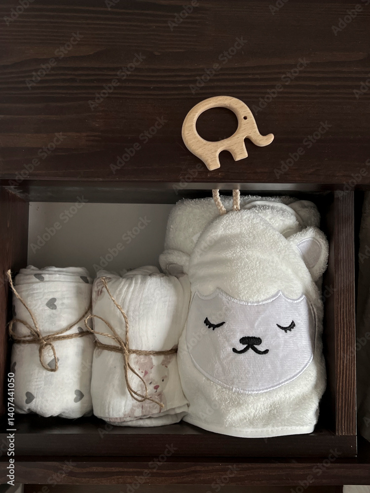 Muslin diapers, a white terry towel in the drawer of the bedside table. A wooden elephant teether is lying on the bedside table. Children's minimalistic accessories for a newborn