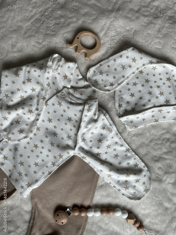 A set of neutral beige children's clothes for discharge. Baby's turtleneck, pants, cap, elephant teether and beads on the bed. Top view