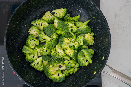 Принти на полотні Fresh broccoli florets cooking in a non-stick pan on a stovetop.
