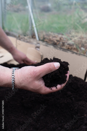 Hand holding compost being put into a raised bed ready for planting