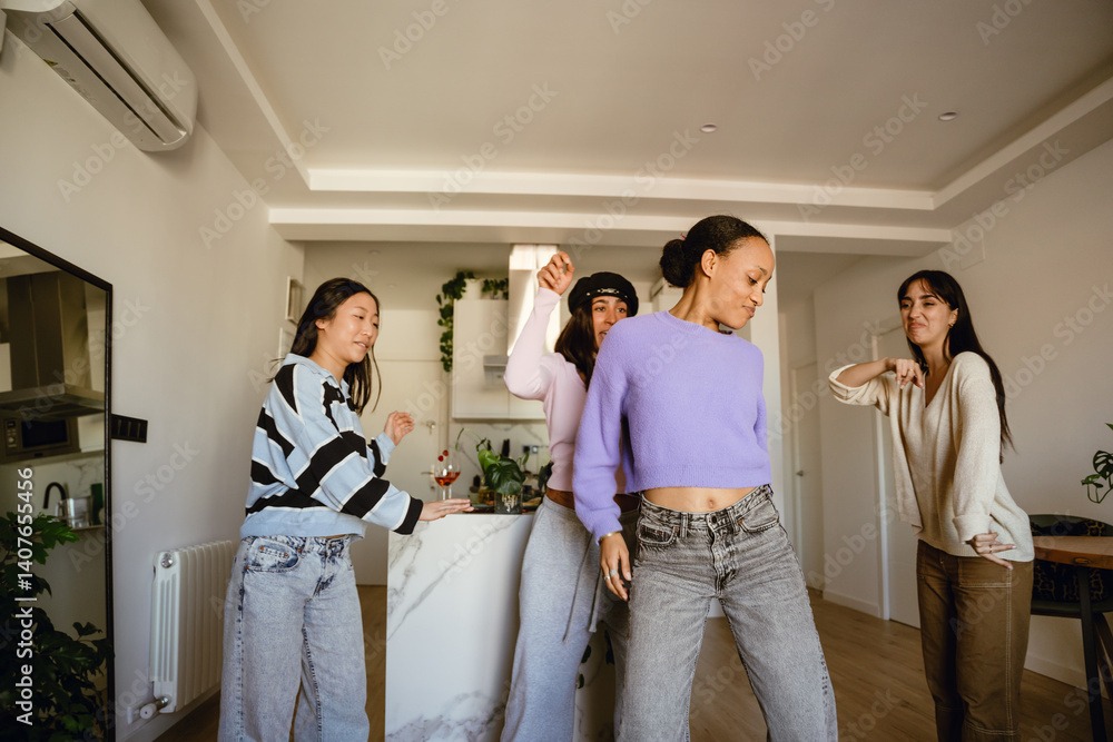 A young African American woman in her mid-20s, dancing cheerfully in her small apartment as her three female friends cheer her on while they're having a party together, wearing casual outfits