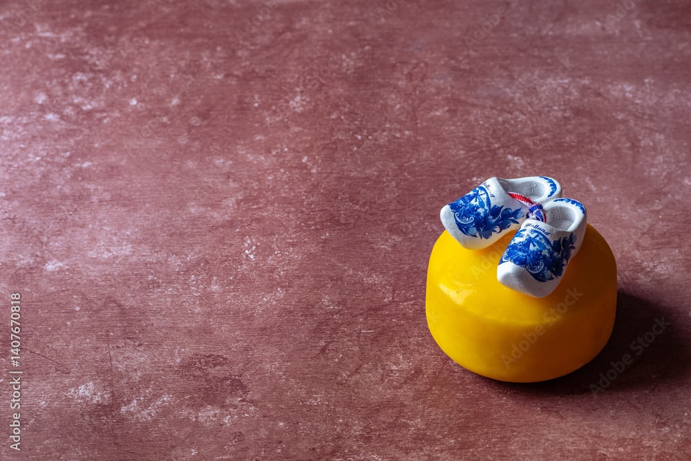 Obraz premium Traditional Dutch gouda cheese wheel and wooden clog shoe against red background. These are iconic to the netherlands.