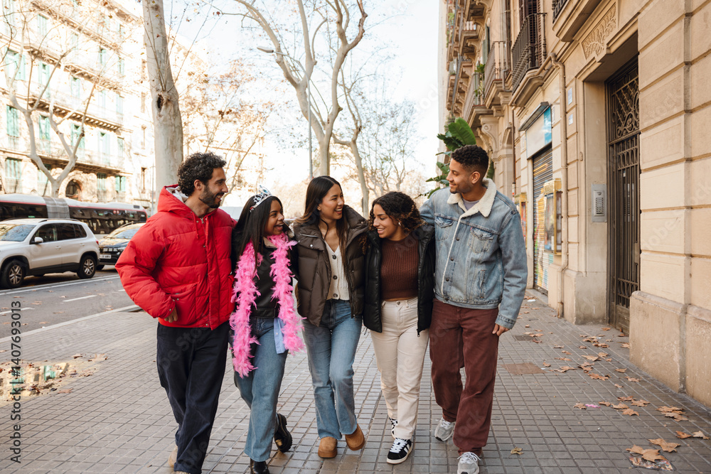 Fototapeta premium A multinational group of young people walking down the street, laughing and celebrating, with a Black woman wearing a tiara and pink feather boa, marking a birthday celebration in an urban setting.