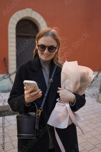Obraz na płótnie A young woman with sunglasses smiling while holding a bouquet of flowers outside a historic building. She appears joyful and the scene captures a beautiful moment in the city. w salonie