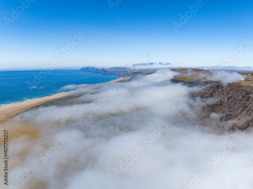 Obraz na płótnie Aerial view of Rauðasandur, Iceland, where golden sands meet turquoise waters, framed by dramatic cliffs and low-hanging clouds under a radiant blue sky. w salonie