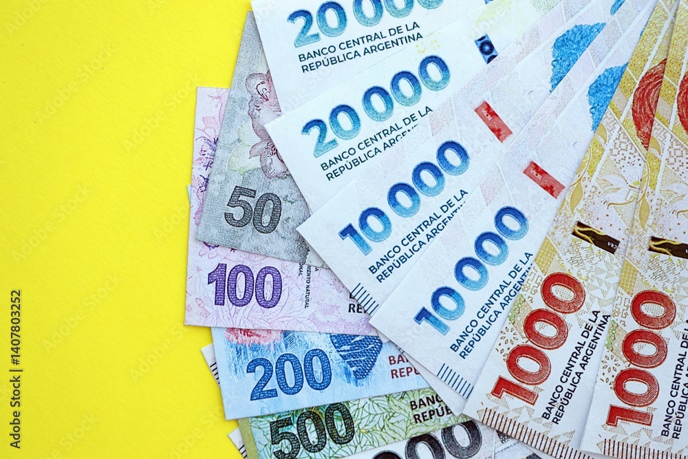 Argentine pesos money bills in big amount lies on yellow color table close up Argentine pesos money bills in big amount lies on yellow color table close up