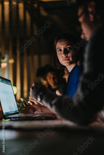 Obraz na płótnie Diverse group of coworkers collaborates intensely on a project in a dimly lit office. The atmosphere is focused and determined as they analyze data and brainstorm ideas to meet an impending deadline. w salonie