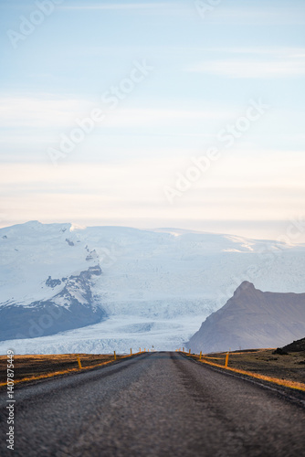 Obraz na płótnie A long empty road leads toward a majestic glacier-covered mountain in Iceland, under a soft pastel sky at sunrise. A breathtaking view of nature's raw beauty and endless adventure. w salonie
