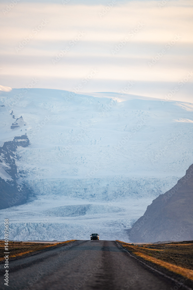 A long empty road leads toward a majestic glacier-covered mountain in Iceland, under a soft pastel sky at sunrise. A breathtaking view of nature's raw beauty and endless adventure.