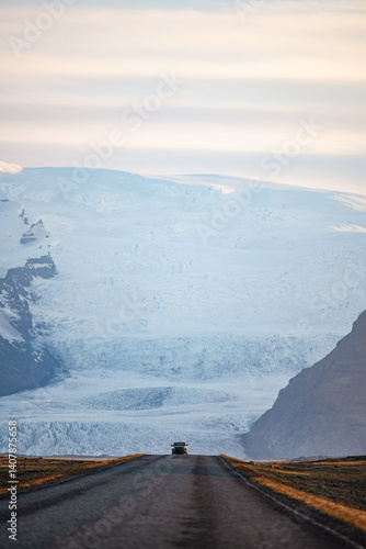 Obraz na płótnie A long empty road leads toward a majestic glacier-covered mountain in Iceland, under a soft pastel sky at sunrise. A breathtaking view of nature's raw beauty and endless adventure. w salonie