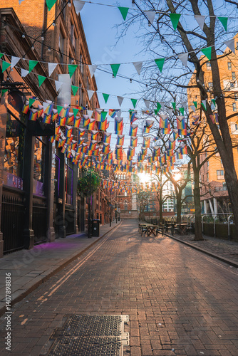 Obraz na płótnie A street in Manchester, England, featuring colorful bunting, historic brick buildings, bare trees, outdoor seating, and a church like structure in the background. w salonie