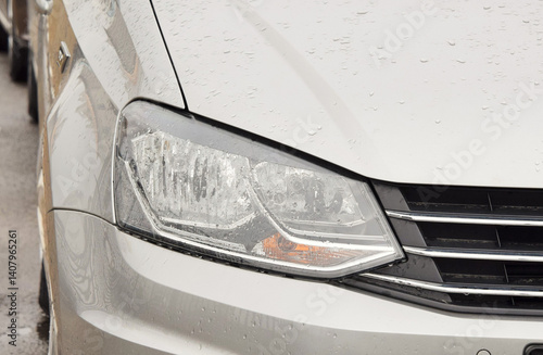 Fotografie in the photo the headlamp of a modern silvery car in rain drops