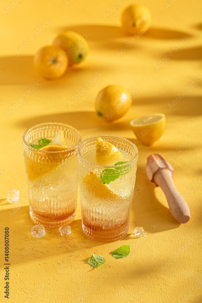 Fresh lemonade with ice on yellow wooden table.