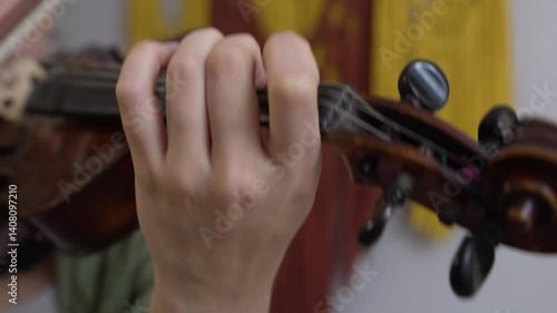 A woman hand moves along the neck of the violin, pinching the strings and chords. Playing the violin at home, close-up