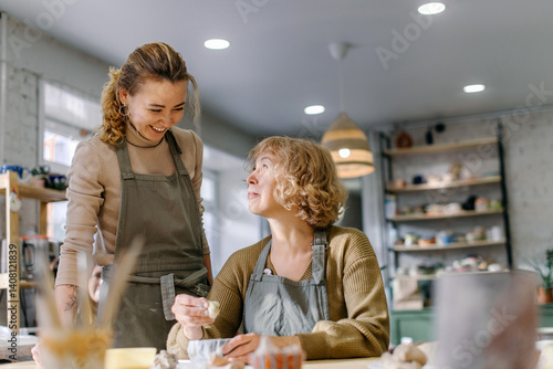 Female artist teaches an elderly woman how to shape clay at a hands-on master class. Happy retired student learns new skills, creating a handmade ceramic bowl