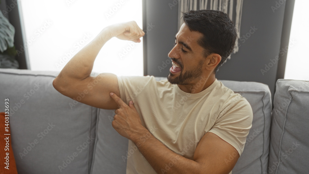 Young hispanic man with beard flexing bicep while sitting on sofa in cozy contemporary living room interior showcasing relaxed confident gesture Young hispanic man with beard flexing bicep while sitting on sofa in cozy contemporary living room interior showcasing relaxed confident gesture