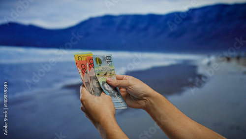 Hands holding australian banknotes on a scenic beach, depicting a financial concept with a seaside backdrop, combining elements of currency and summer relaxation.
