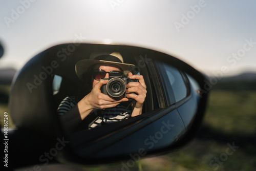A girl traveller in a straw hat takes a photo of herself in a car's side mirror. Freedom vibe
