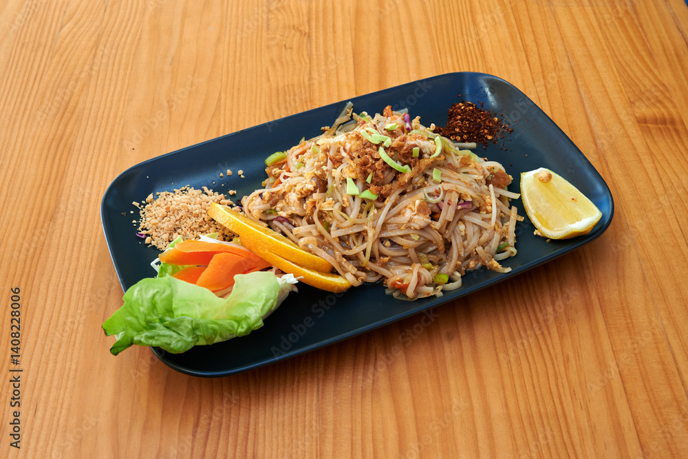 A plate of food with noodles, carrots, and an orange. The plate is on a wooden table