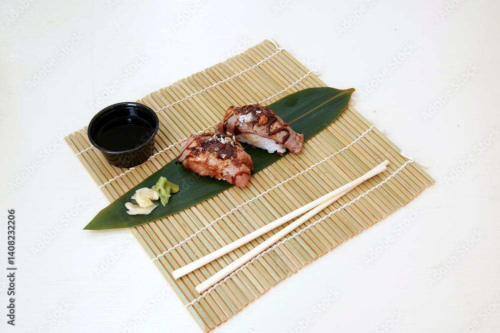 A plate of sushi with soy sauce and wasabi on a bamboo mat. The sushi is on a leaf and is accompanied by chopsticks