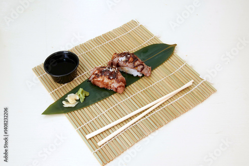 Obraz na płótnie A plate of sushi with soy sauce and wasabi on a bamboo mat. The sushi is on a leaf and is accompanied by chopsticks w salonie