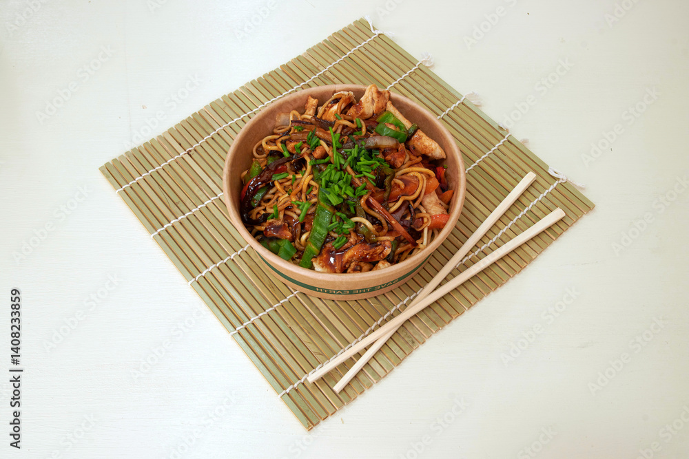 A bowl of food with chopsticks on a bamboo mat. The food is a mix of noodles and meat