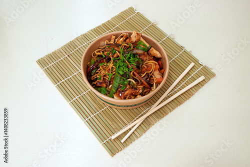 Obraz na płótnie A bowl of food with chopsticks on a bamboo mat. The food is a mix of noodles and meat w salonie