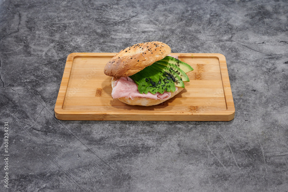 A sandwich with avocado and ham on a wooden board. The sandwich is cut in half