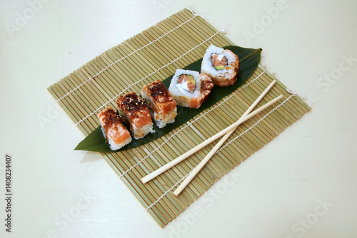 Obraz na płótnie A plate of sushi with chopsticks on a bamboo mat. The sushi is made with salmon and avocado w salonie