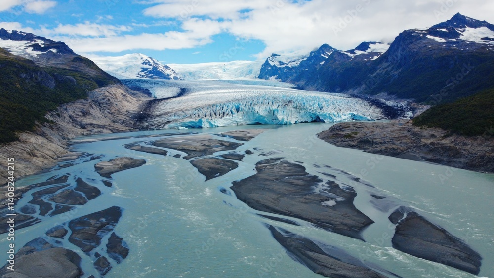 Scenic view of glacial bay with floating ice, waterfalls and towering peaks in the distance.